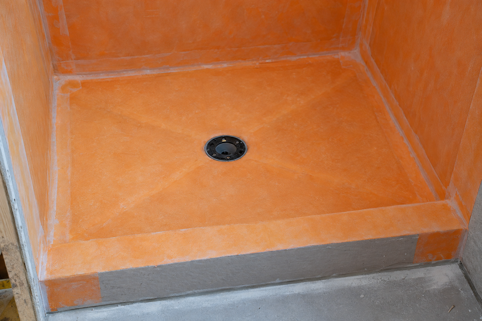Sloped shower pan coated in orange waterproofing membrane with the drain at its center