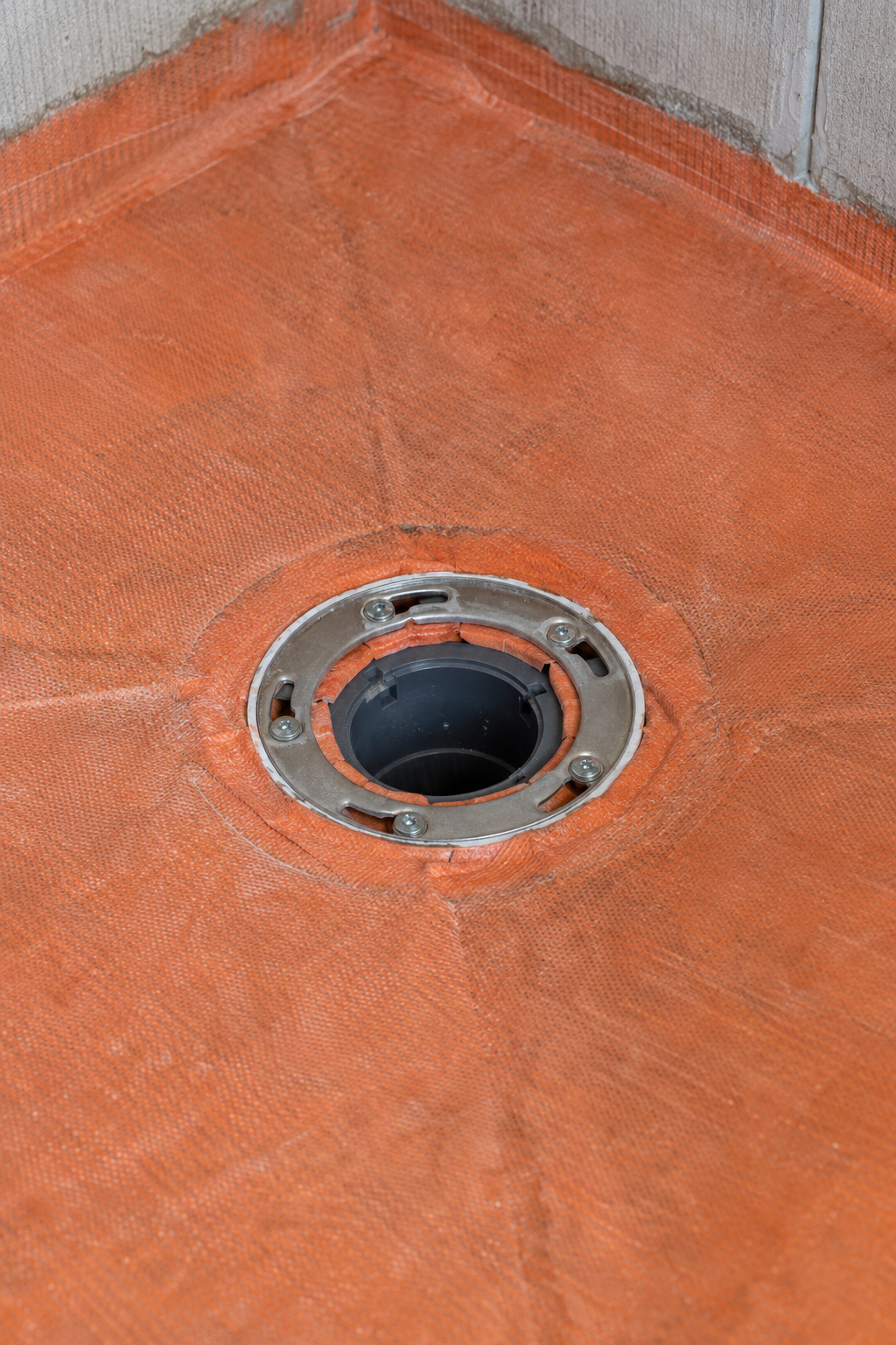 Shower drain clamping ring bolted down over a waterproofing membrane on a sloped shower pan